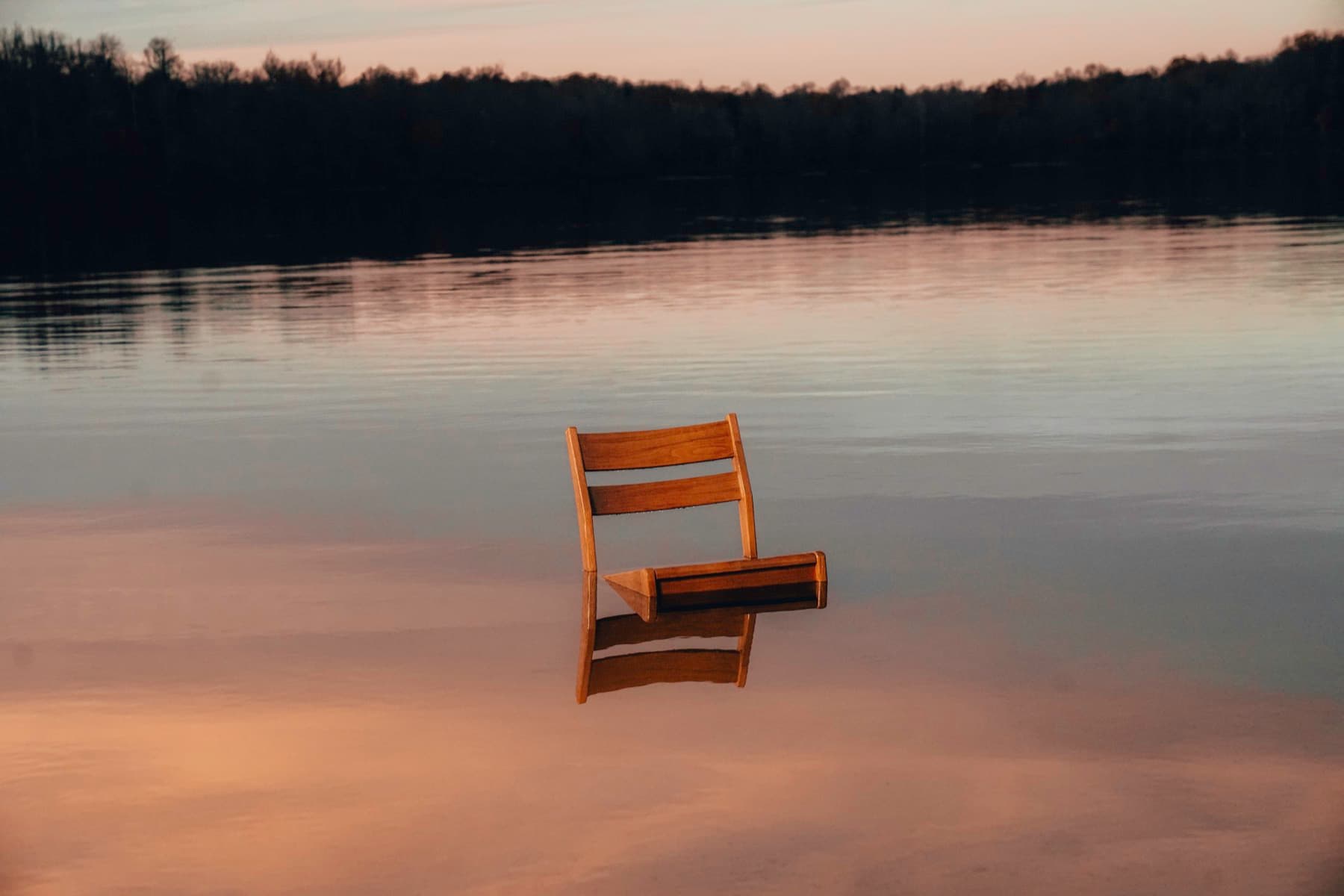 Wooden chair partially submerged in still water at dusk.